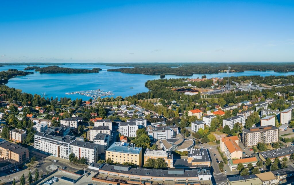 Ilmakuva kesäisestä kaupungista, jossa näkyy Lohjan keskusta, asuinrakennuksia, venesatama ja järvimaisema taustalla.